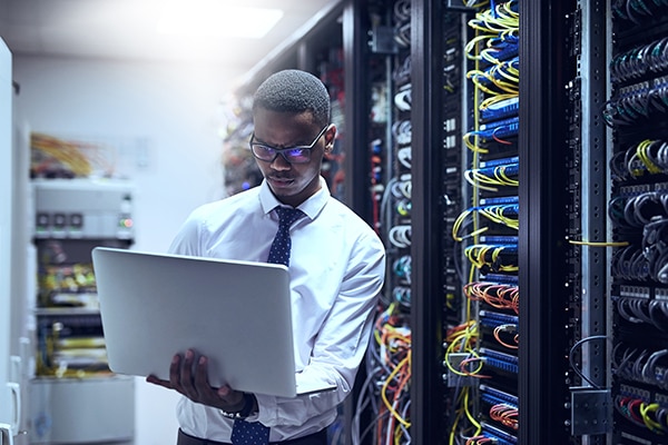 Man on a laptop in a server room Image of man on a laptop in a server room