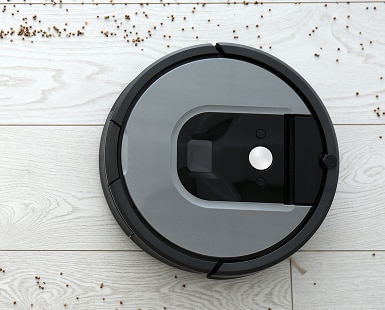 Overhead view of robot vacuum on a white wood floor cleaning up debris