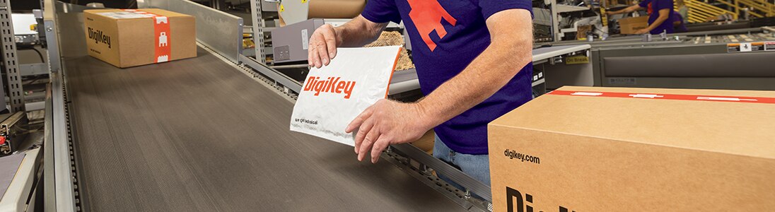 A flat-mailer envelope held by a man in a purple shirt who is about to place it on a conveyor belt