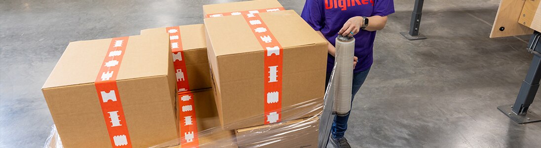 A woman in a purple DigiKey shirt wrapping a pallet loaded with boxes in clear plastic wrapping