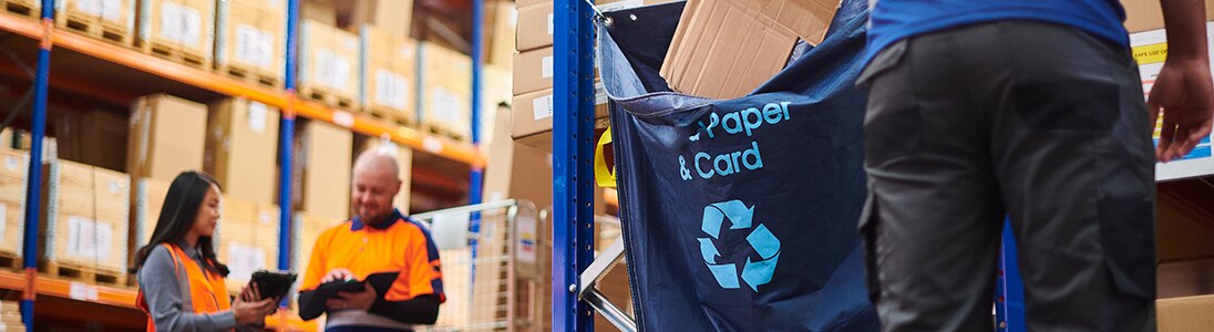 A blue pouch for cardboard recycling hanging from shelving in a warehouse