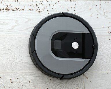 Overhead view of robot vacuum on a white wood floor cleaning up debris