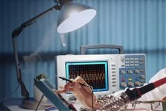Woman using soldering iron and oscilloscope